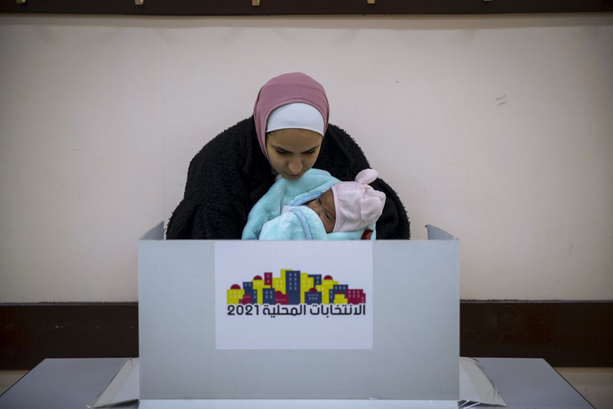 A Palestinian woman holds a baby as she casts her vote at a polling station during municipal elections, in the West Bank village of Kifl Haris, Saturday, Dec. 11, 2021. Palestinians took part in rare municipal elections across the occupied West Bank on Saturday, following months of simmering anger towards their government and the cancellation of promised parliamentary and presidential elections earlier this year. (AP Photo/Majdi Mohammed)