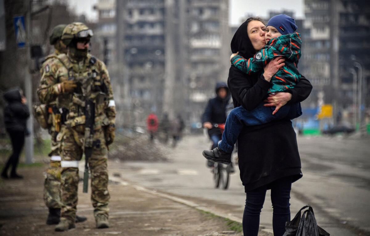 A woman holds and kisses a child while two soldiers near her.