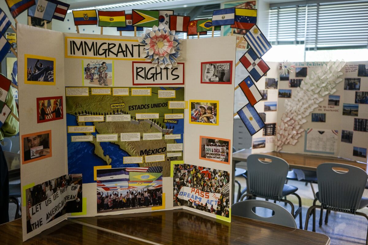 A project  board in a classroom features flags of nations and the words Immigrant Rights above a map and photos on the sides 