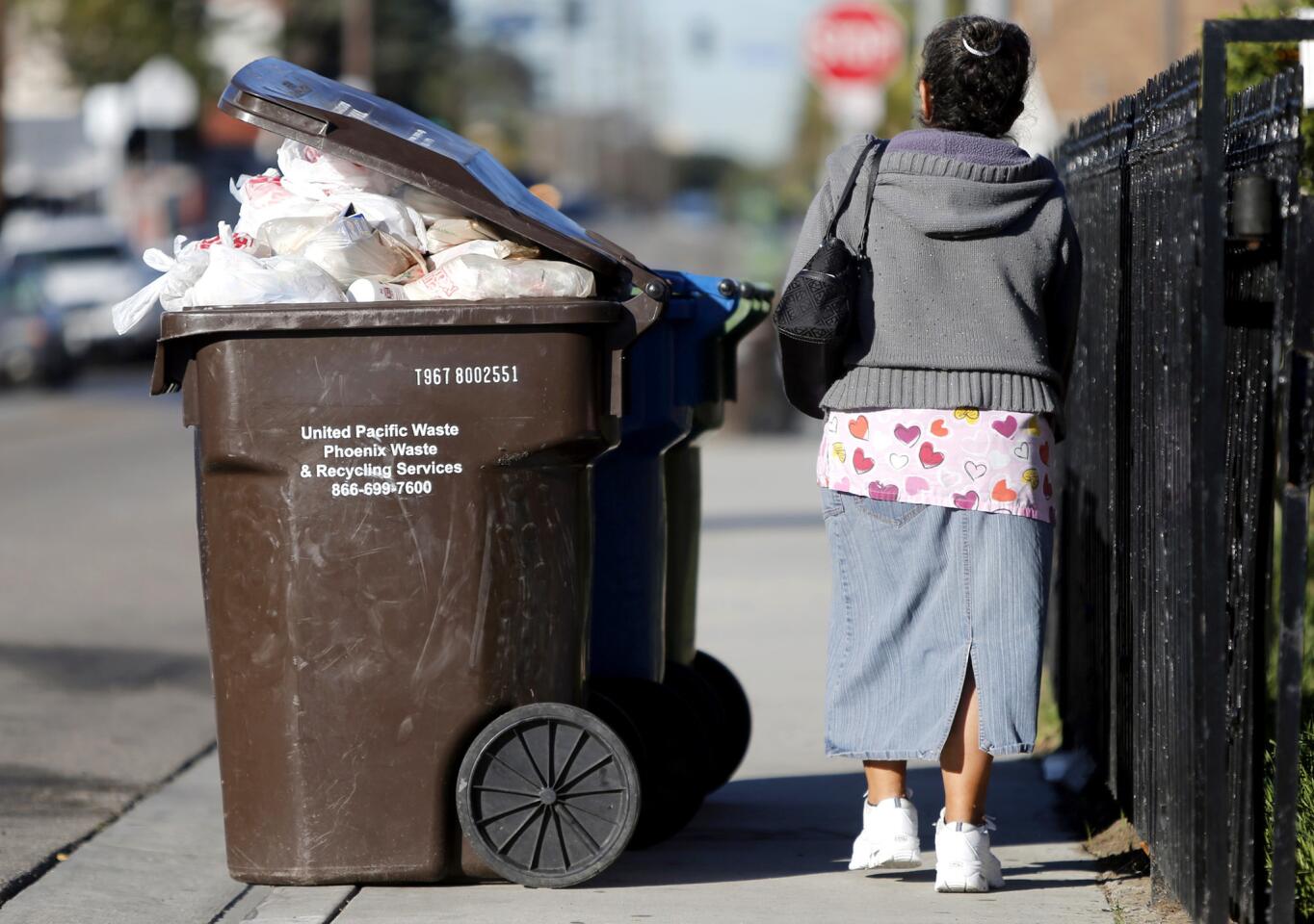 A pedestrian shares the sidewalk with a packed trash container.