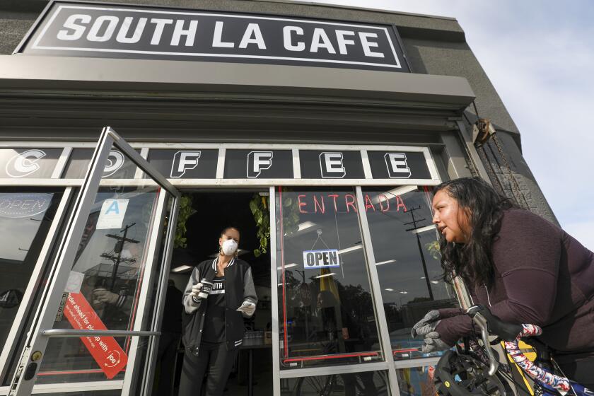 LOS ANGELES, CA - MARCH 28, 2020 - Celia Ward-Wallace, left, brings a take-out order to Sandra Flores at South LA Cafe. The coronavirus pandemic is threatening South LA's renaissance, which has seen a boom in the opening of small, black-owned cafes, coffee shops like South LA Cafe in the last couple of years. The owners of South LA Cafe fear they might not be able to hang on if this shutdown persist. (Irfan Khan / Los Angeles Times)