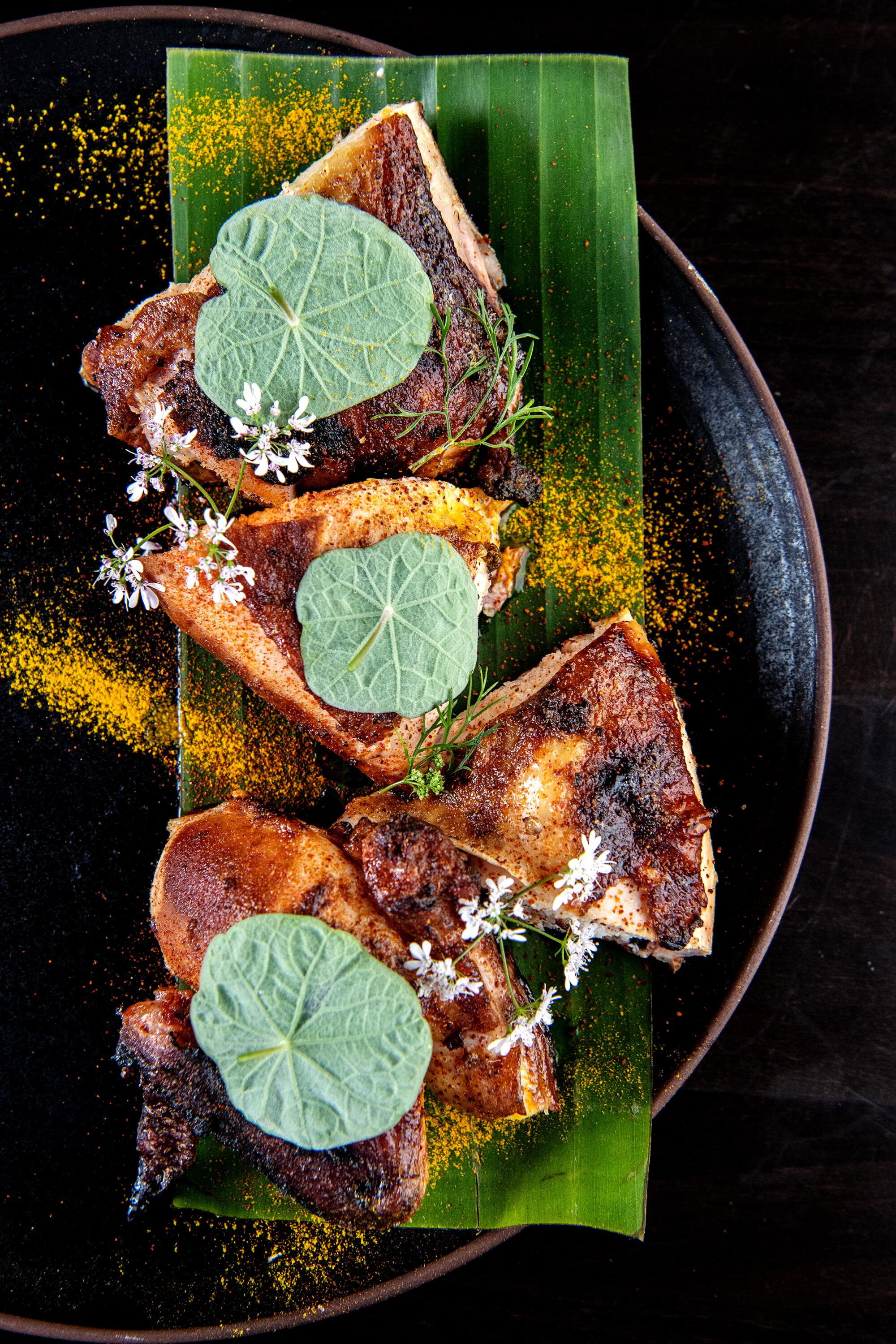 Pieces of smoked chicken sit atop part of a green leaf on a black plate.