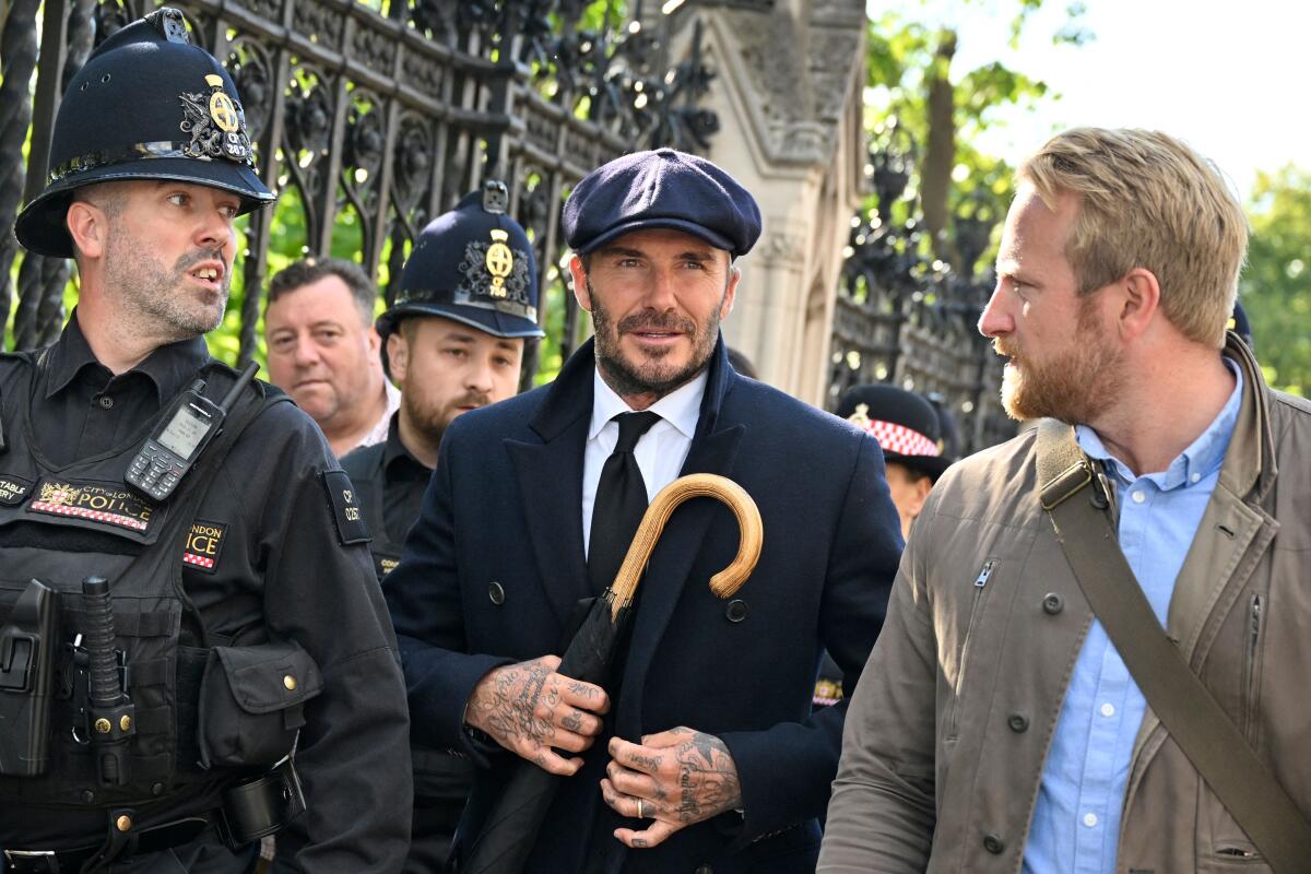 A man in a coat, suit and cap carries an umbrella near police after paying his respects to the late Queen Elizabeth II