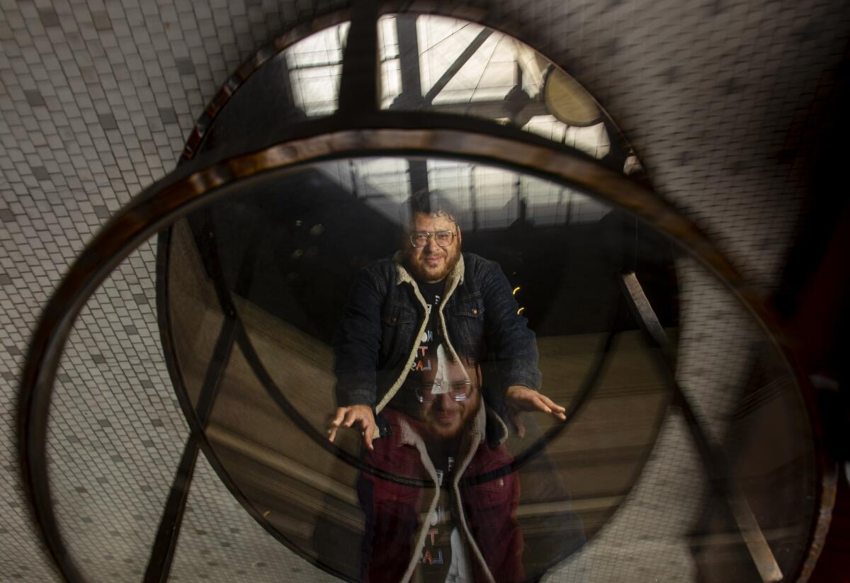 christopher oscar peña is seen in the reflection of a mirrored glass