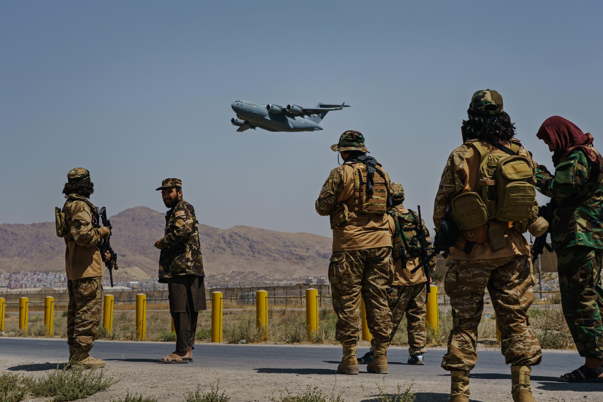 A C-17 Globemaster aircraft takes off as armed men watch.