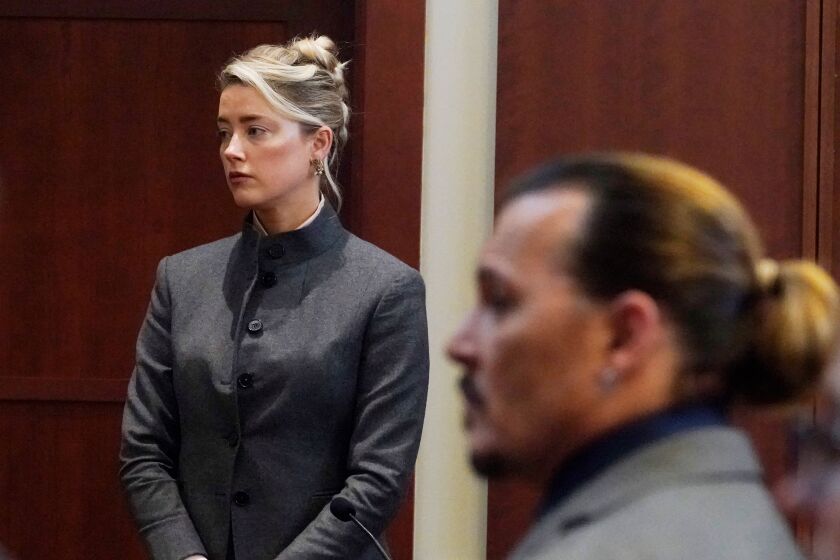Amber Heard standing in a courtroom as Johnny Depp sits in the foreground.