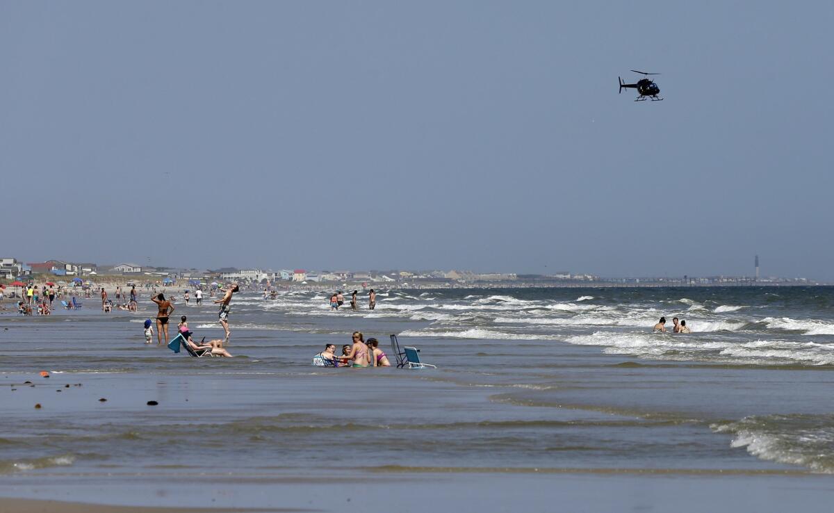 A helicopter flies close to the water as vacationers relax on the beach in Oak Island, N.C., on June 15, a day after a 12-year-old girl and a 16-year-old boy were seriously injured in shark attacks there.