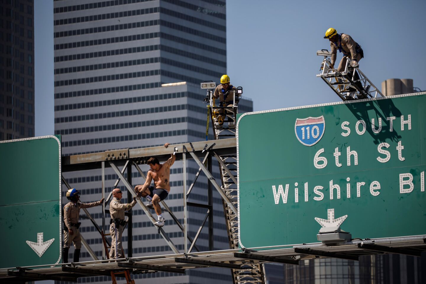 Firefighters and California Highway Patrol officers attempt to remove a shirtless man from a sign over the 110 Freeway in downtown Los Angeles.