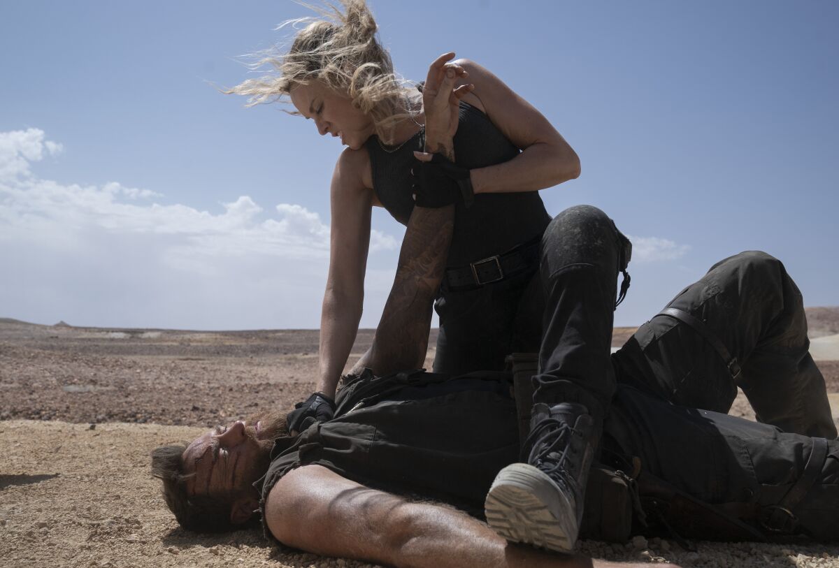 A woman holds a man down on the dirt