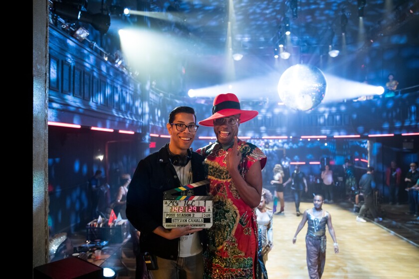"Pose" co-creator, writer and director, Steven Canals, poses with a director's clapperboard on the set of the FX show. He smiles with actor Billy Porter, as bright lights shine behind them.
