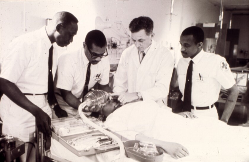 Three men closely observe another man demonstrating medical equipment