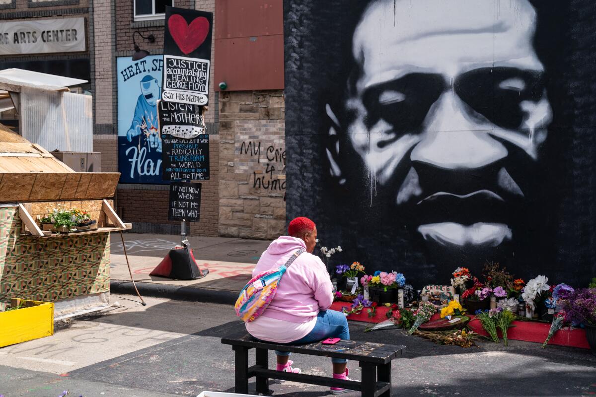 Myisha T. Hall of Las Vegas sits on a bench in front of a large mural depicting George Floyd.