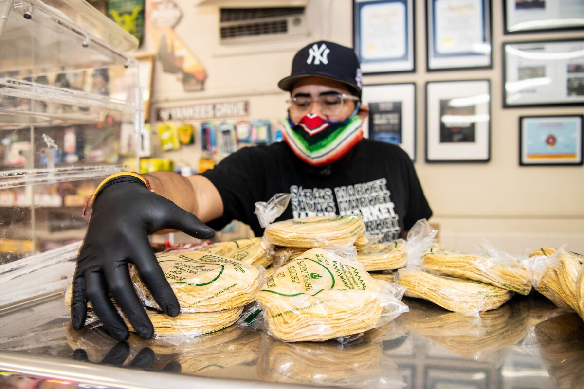 While wearing a mask and gloves, Sara's Market co-owner Steven Valdez sorts tortillas.