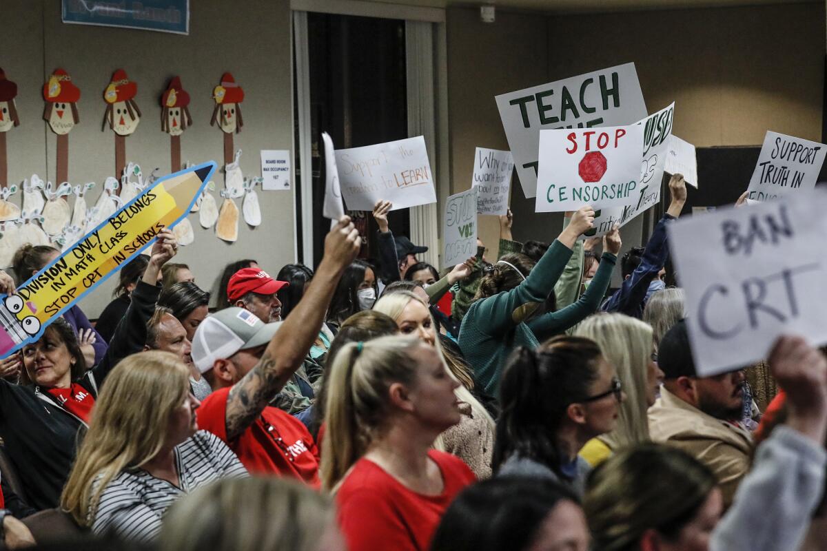 A mix of people hold up signs at a public school board meeting.