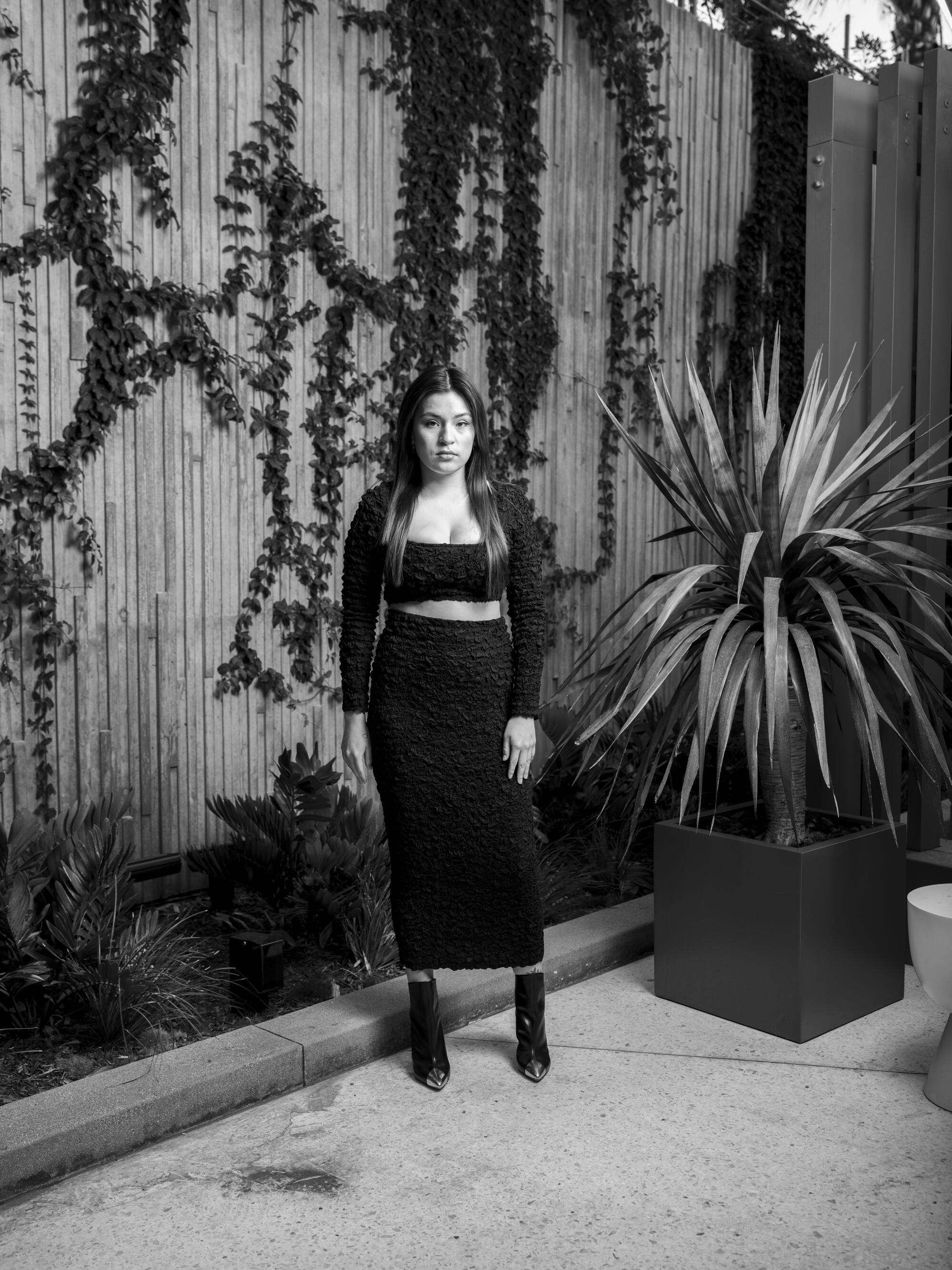 A young woman in a black, two-piece dress poses for a portrait in a courtyard.