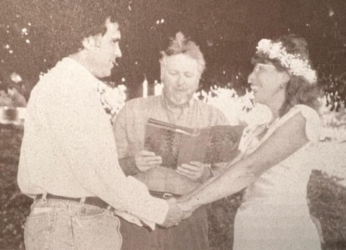 Two people hold hands as another person reads from a book.