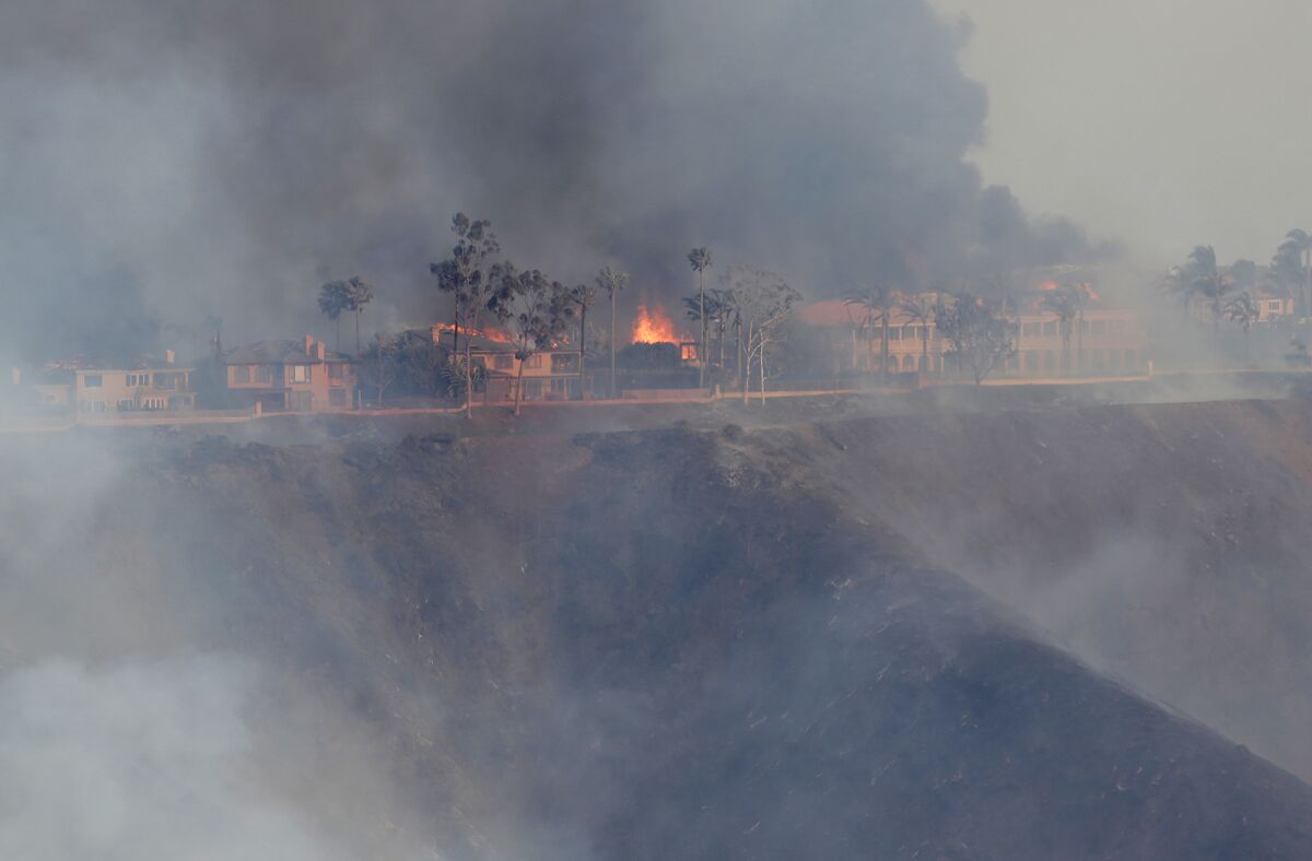 Thick, dark smoke rises from burning homes on top of a ridge