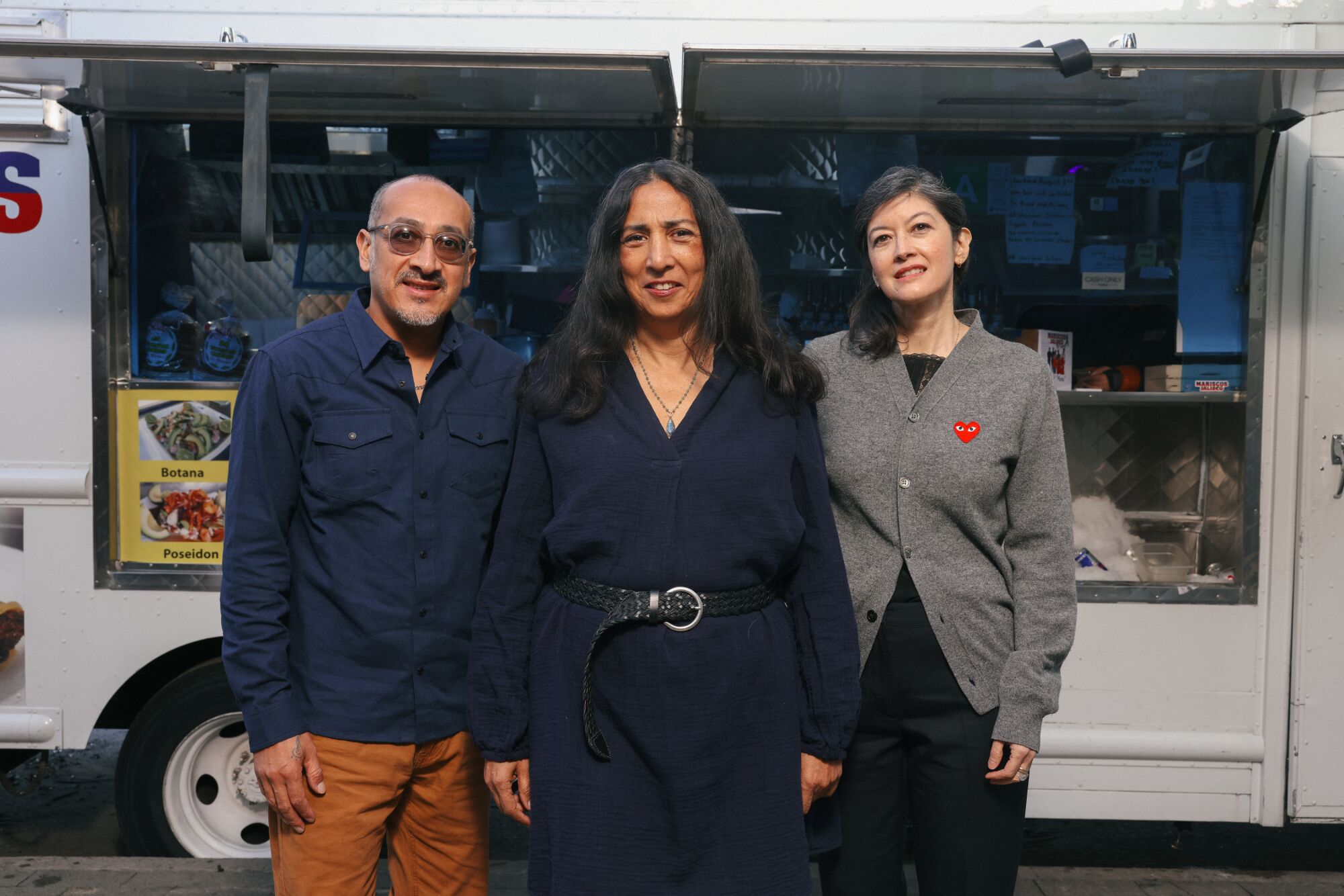 A man and two women pose for a picture in front of a food truck.