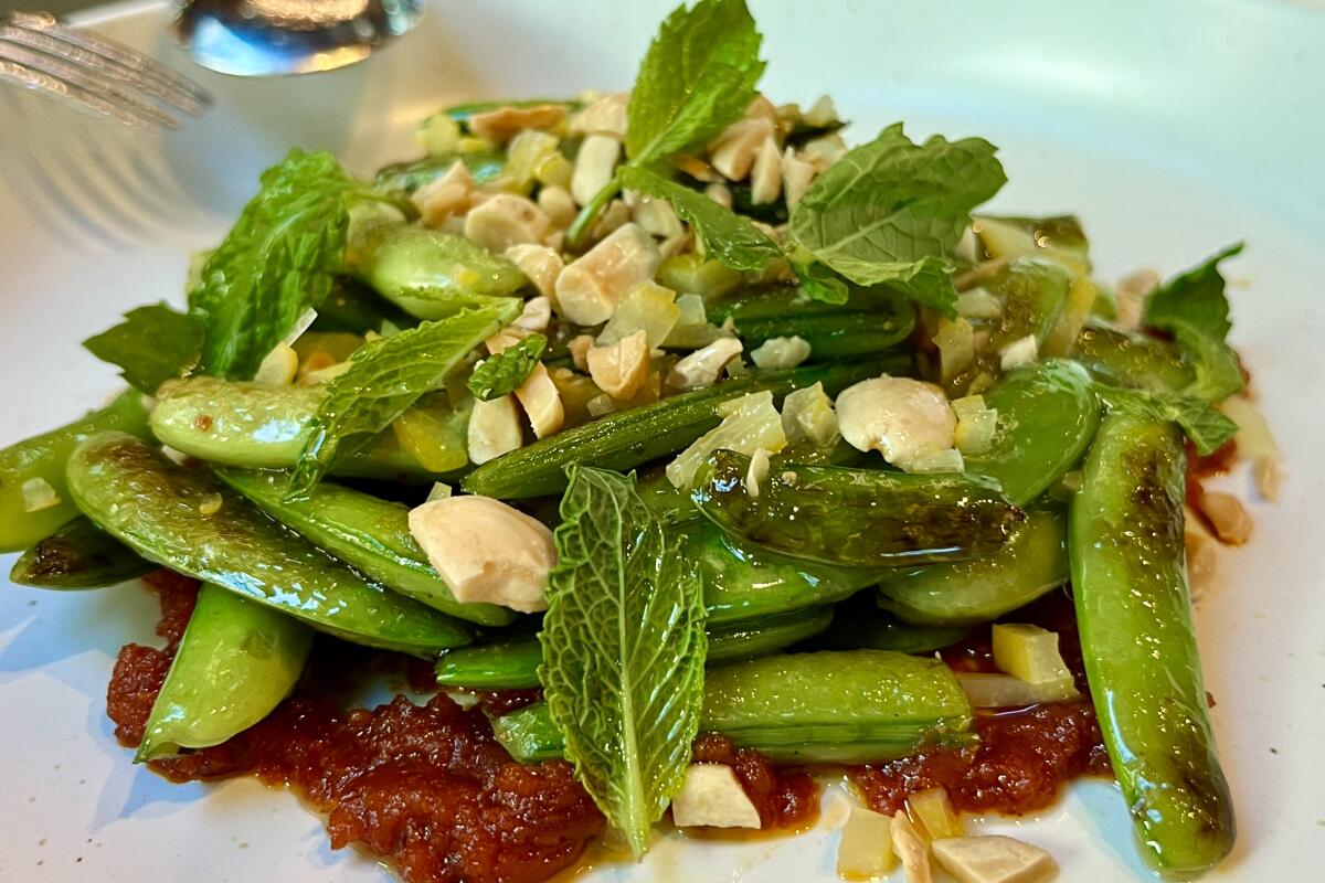 Blistered snap peas piled on tomato sauce, sprinkled with almonds and mint leaves