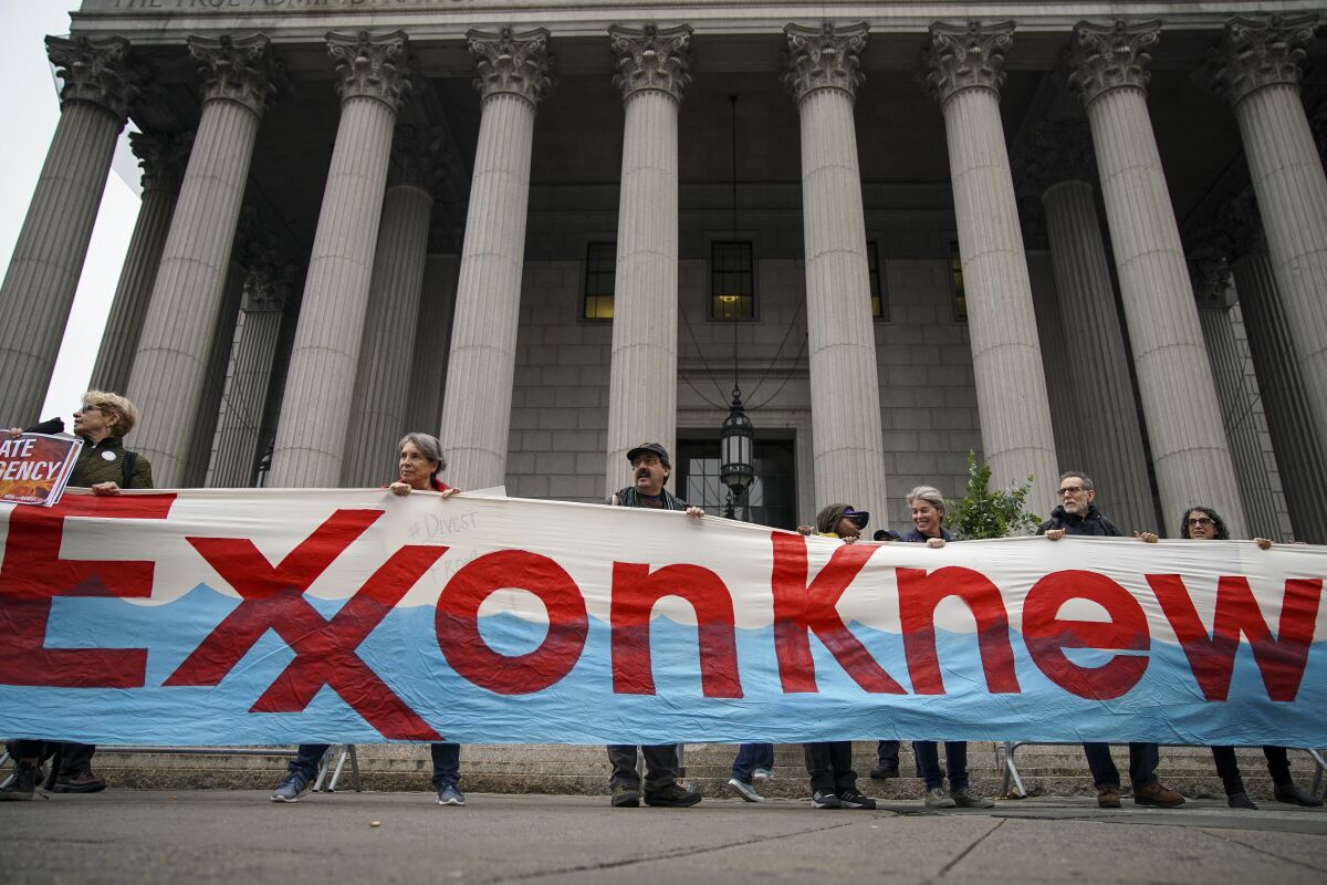 Protestors hold a banner reading “Exxon knew” outside an ornate government building.