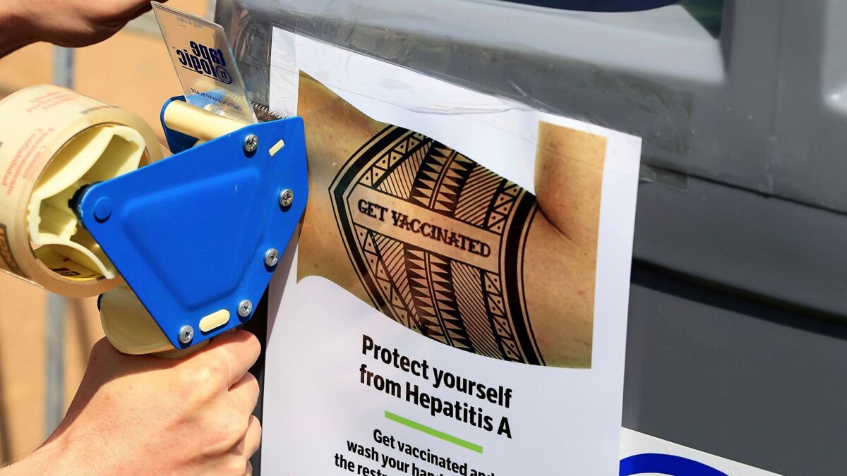 A worker tapes signage telling people to get vaccinated to protect themselves against Hepatitis A in downtown San Diego. (Eduardo Contreras / AP)