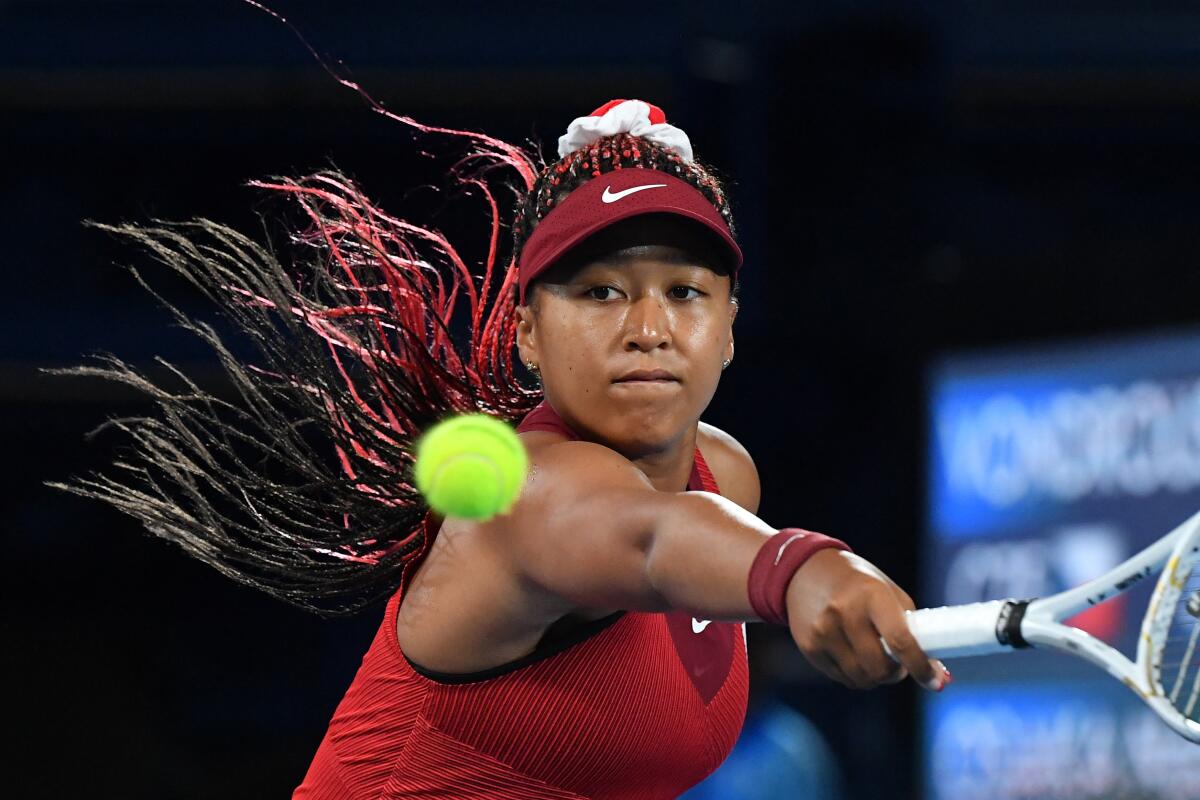 A tennis player in a red visor and blouse fiercely returns a ball, portrayed in mid-swing.