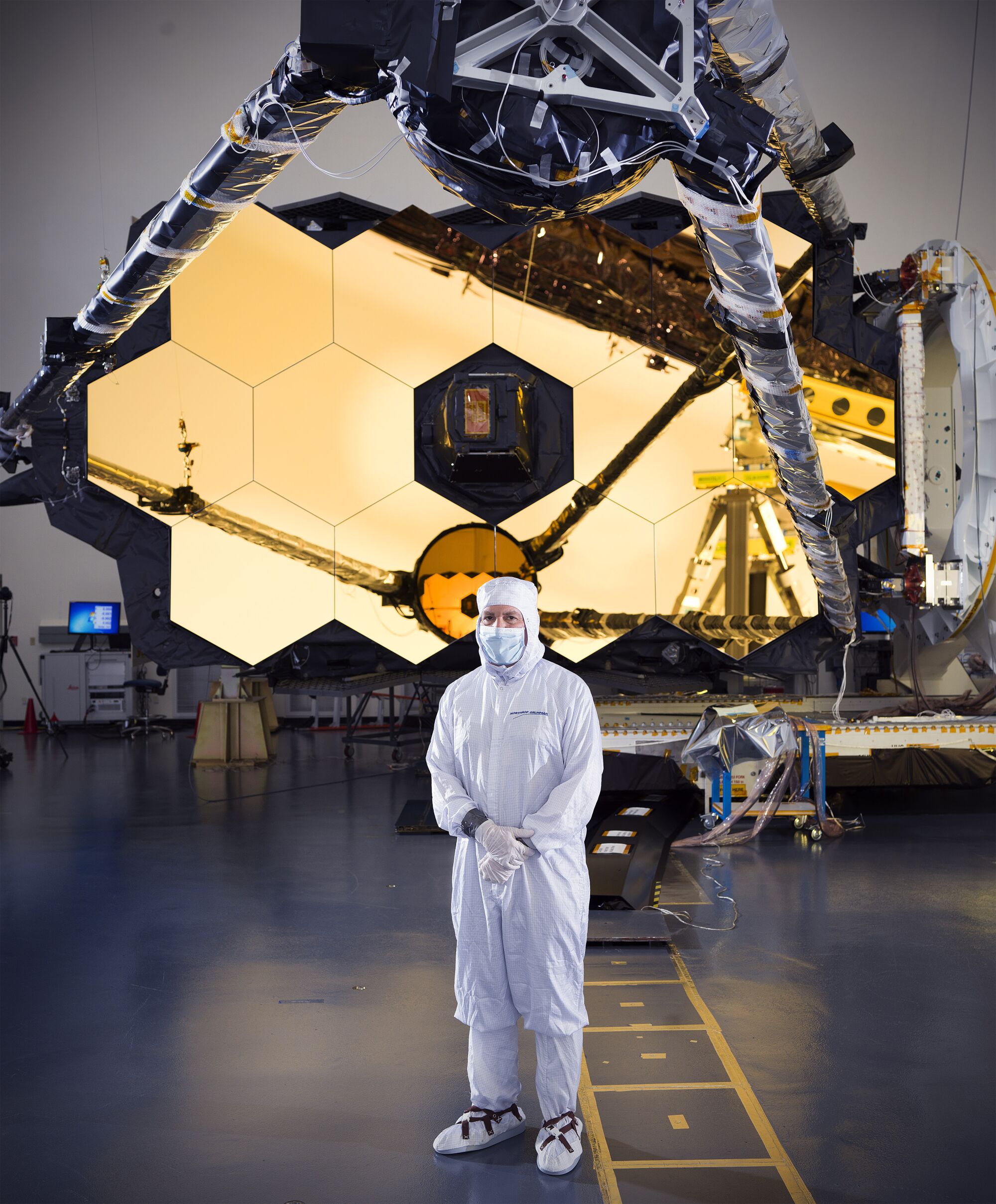 A man in a sanitary white outfit stands in front of the telescope mirror