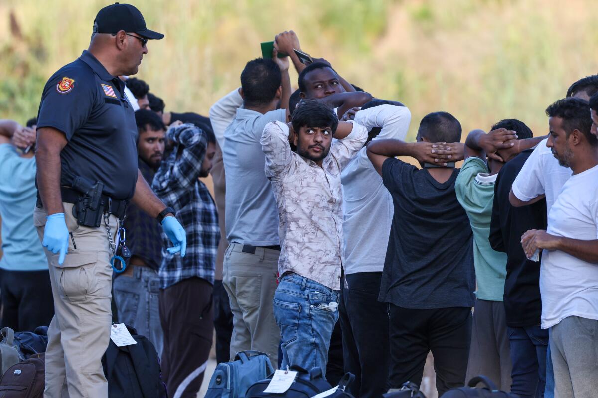 A Border Patrol agent talks to migrants who stand or kneel with hands behind their heads