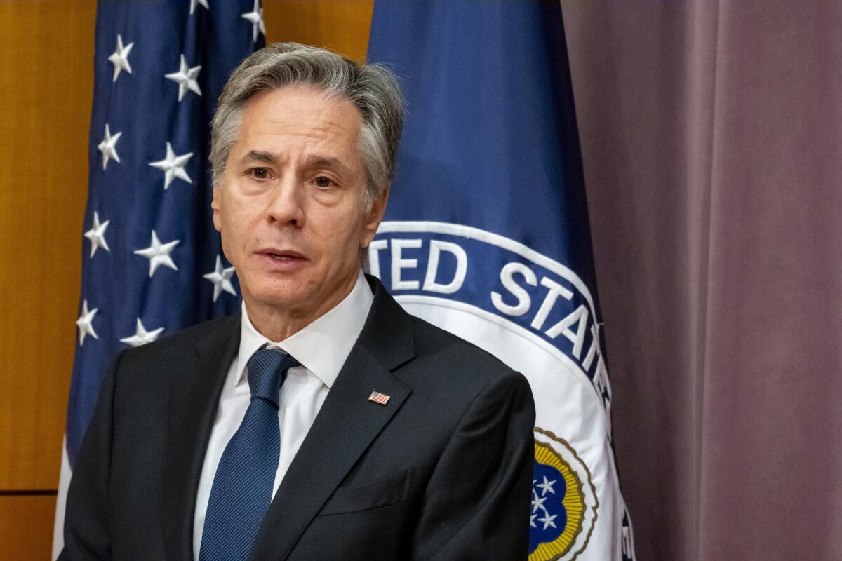 Secretary of State Antony J. Blinken speaks, with two flags behind him 