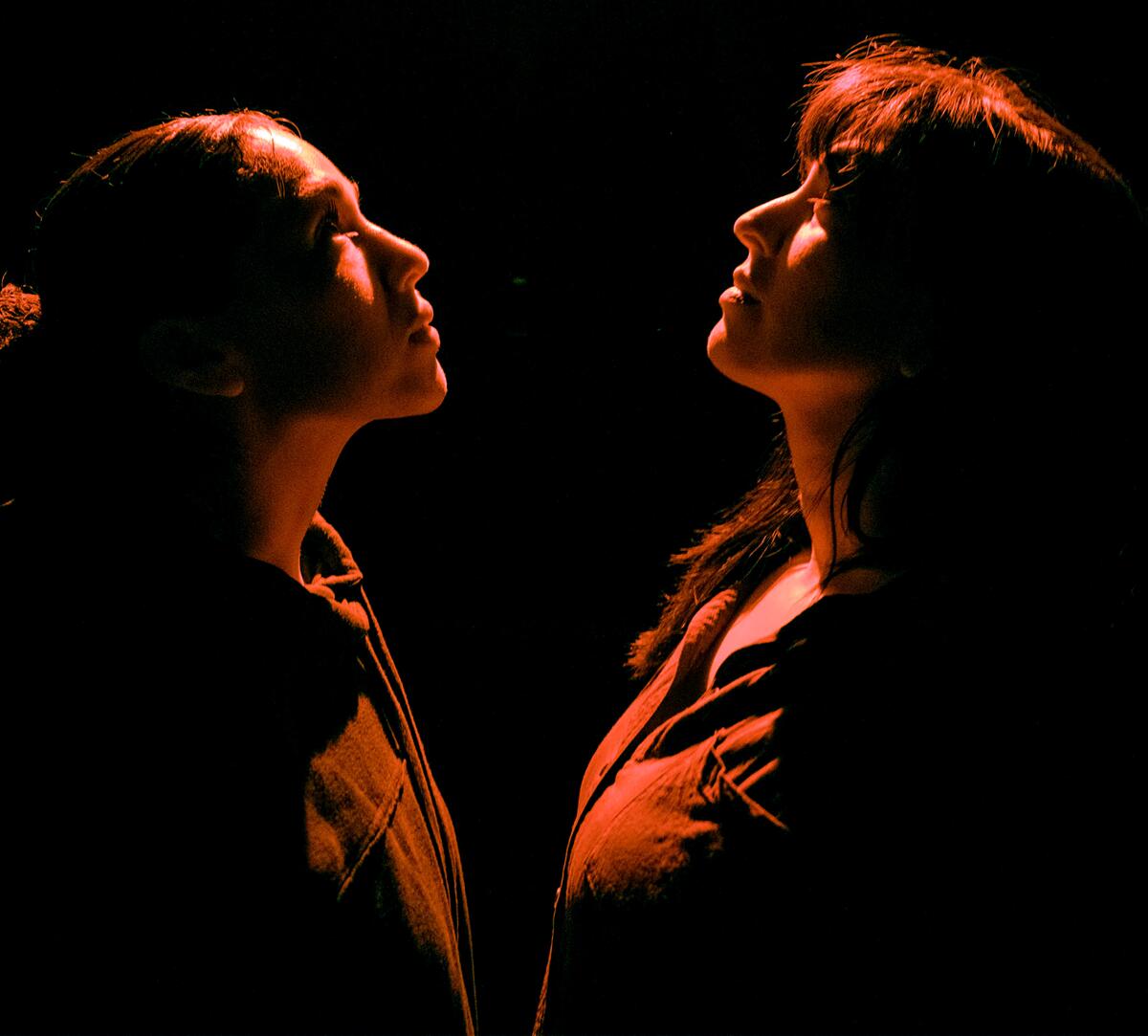 Two women standing in front of each other, looking up to the ceiling. 