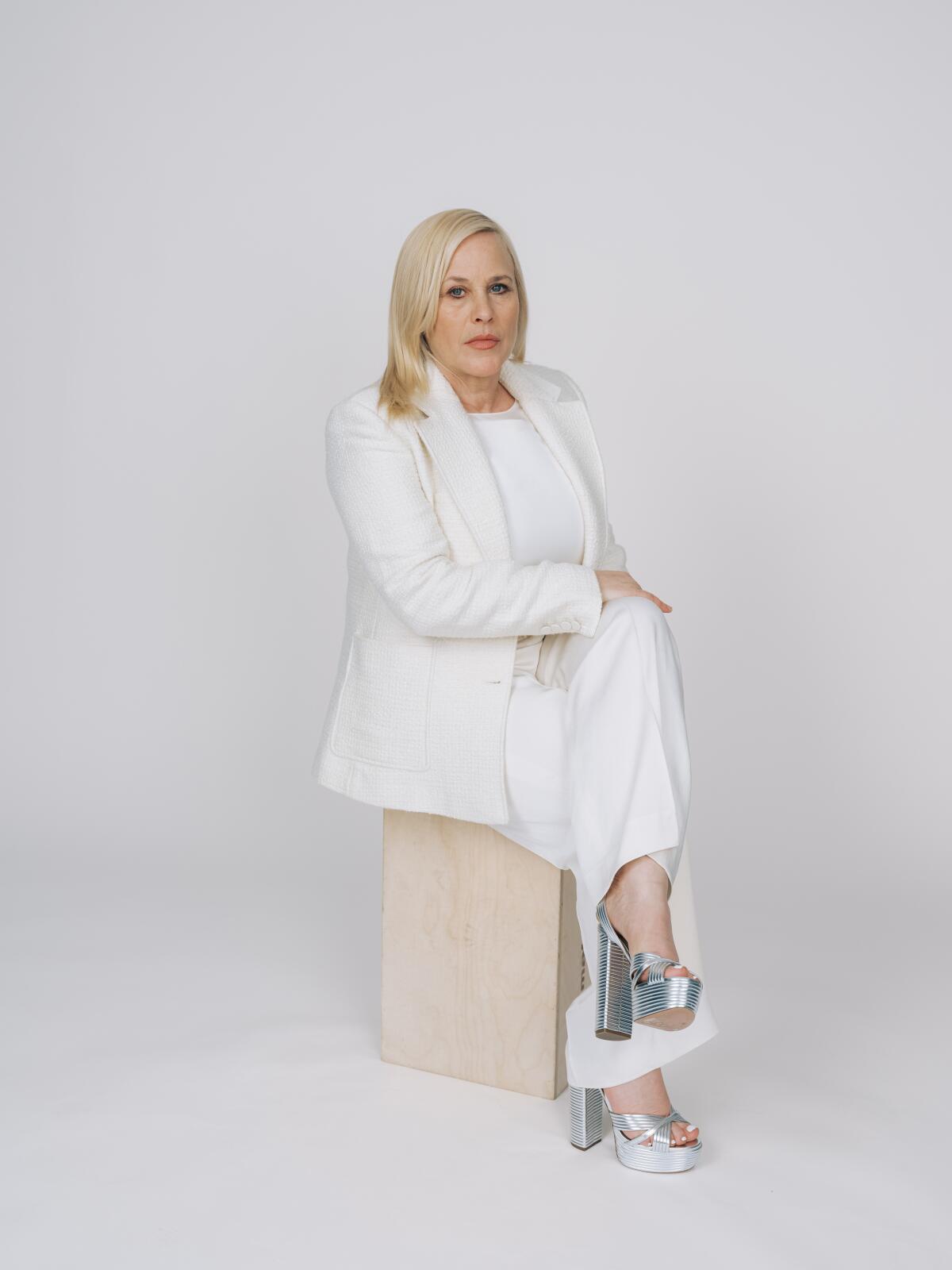 Patricia Arquette in a white suit and blouse and silver platform heels.
