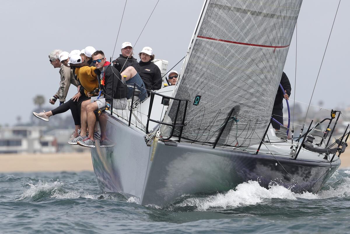 A crew sit on the rail of their boat.