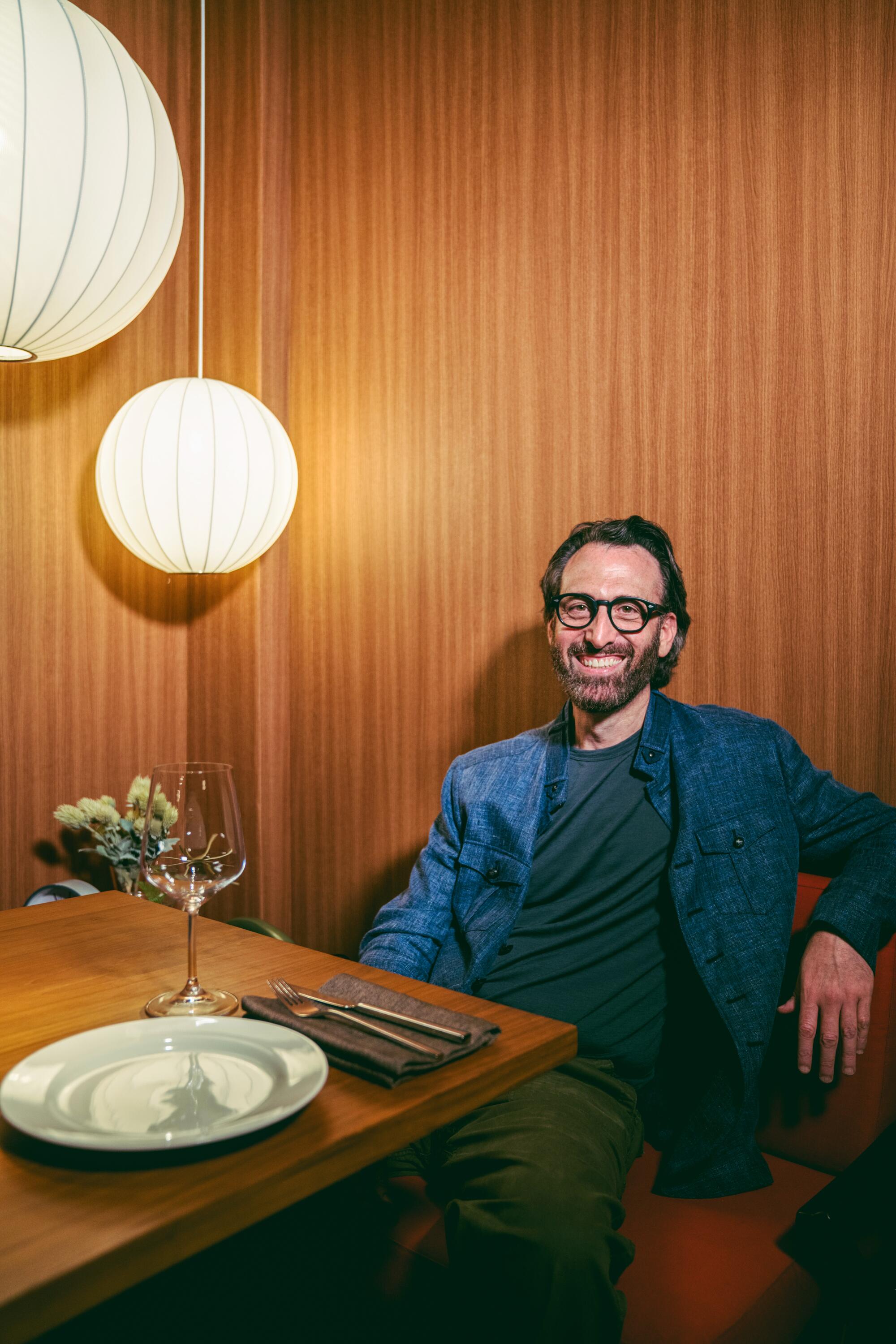 A man sits and smiles at the camera at a restaurant.