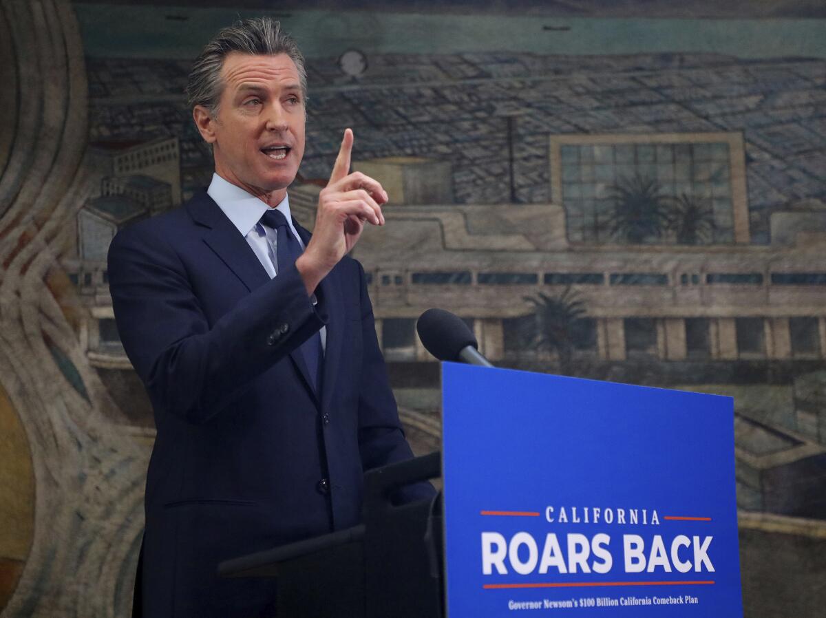 California Gov. Gavin Newsom holds up an index finger while at a lectern with a sign on it saying California roars back.