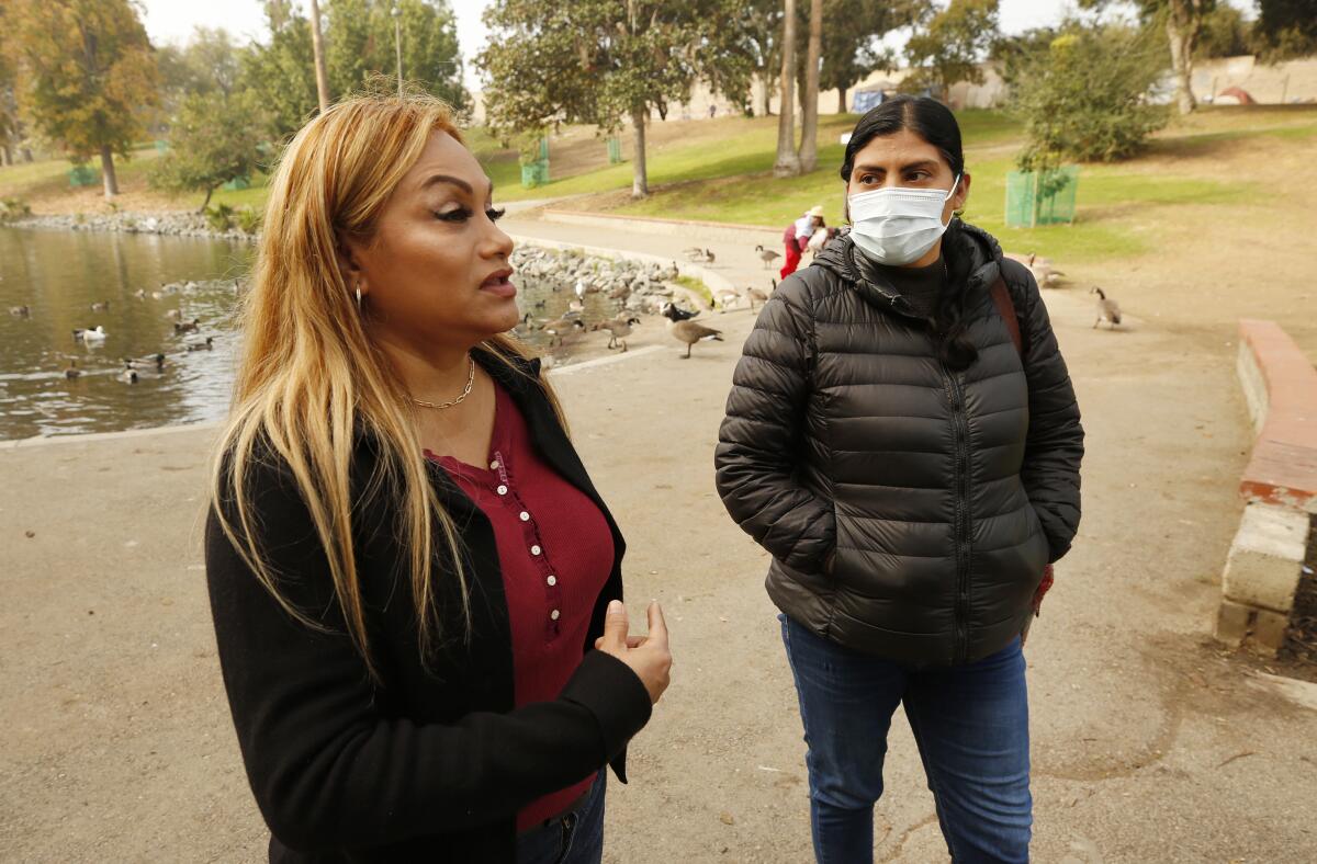 Two women stand in a park near water.