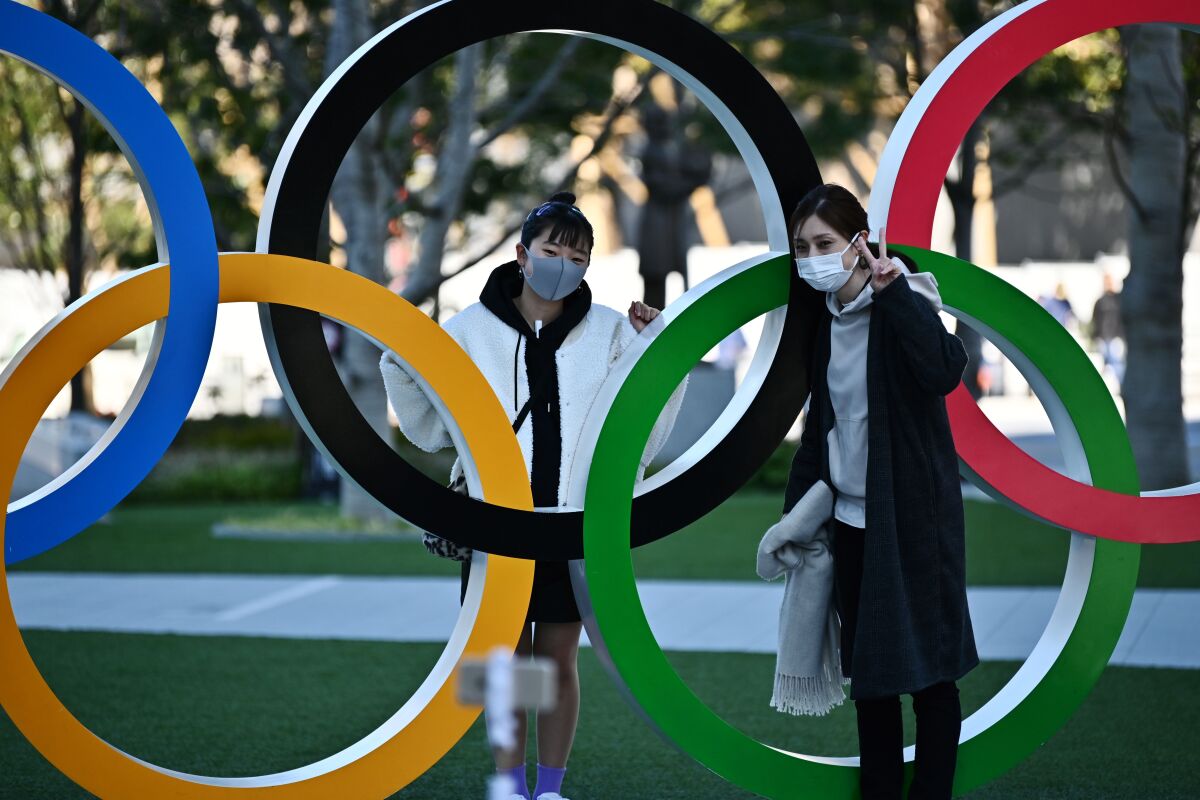 Mask-clad people pose with an Olympic rings display in Tokyo on Friday