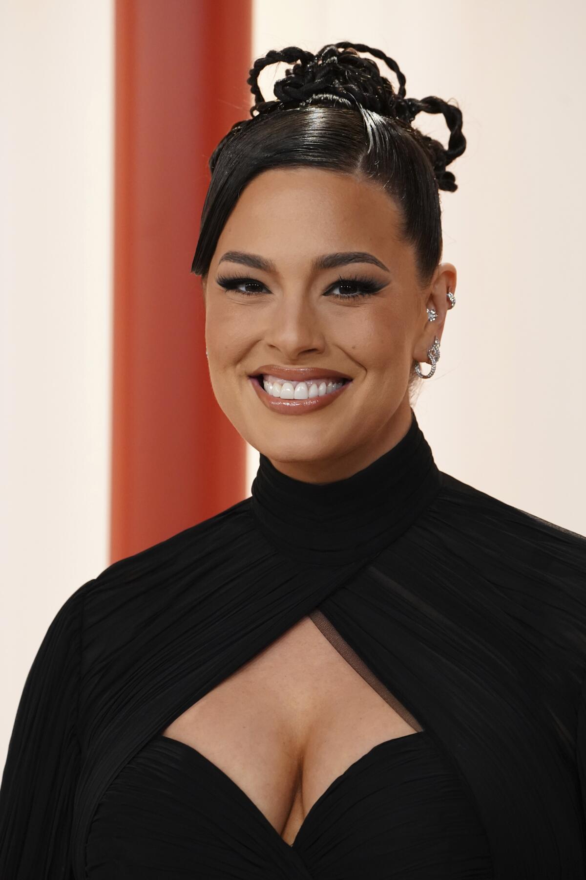 A woman with a braided bun in a black gown smiles.