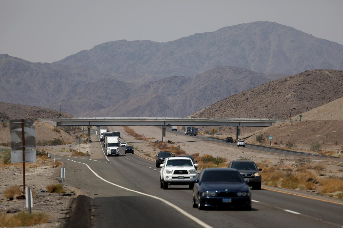 Cars and trucks traverse a highway through a mountainous desert.