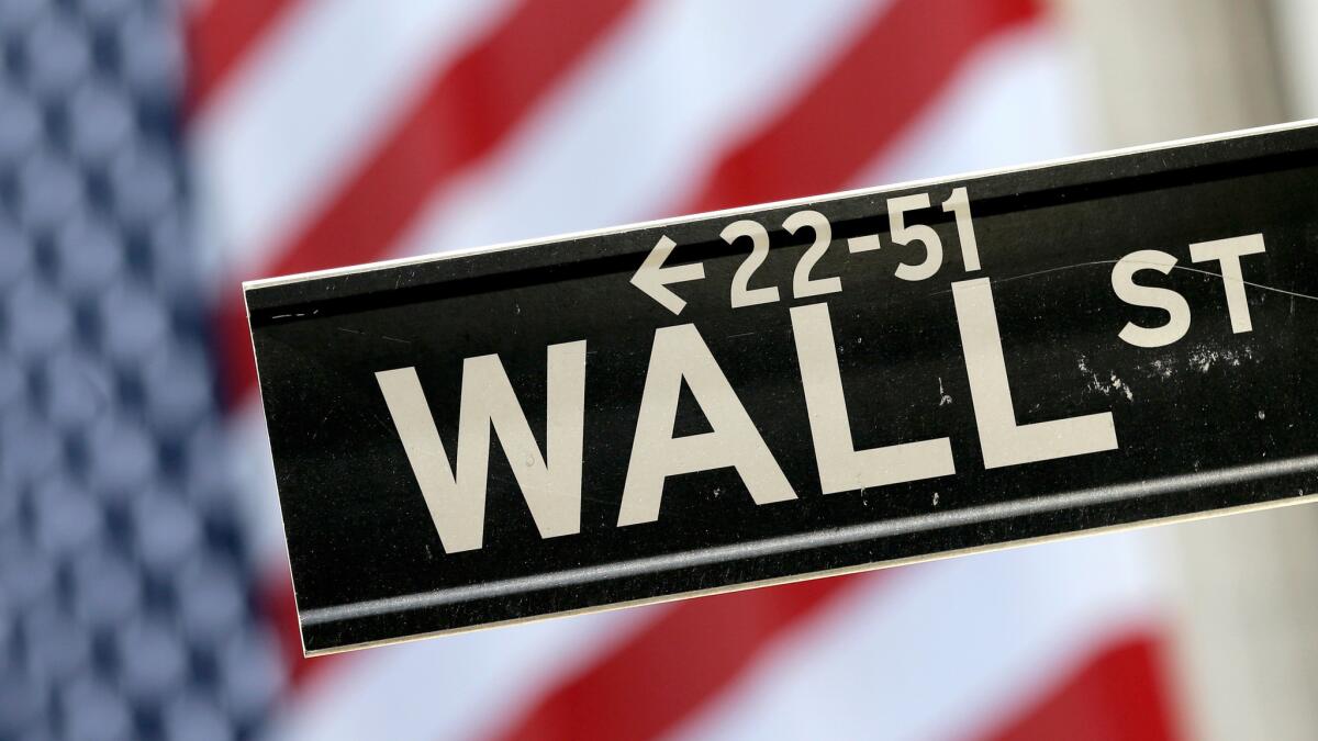 A Wall Street sign is framed by a U.S. flag hanging on the facade of the New York Stock Exchange.