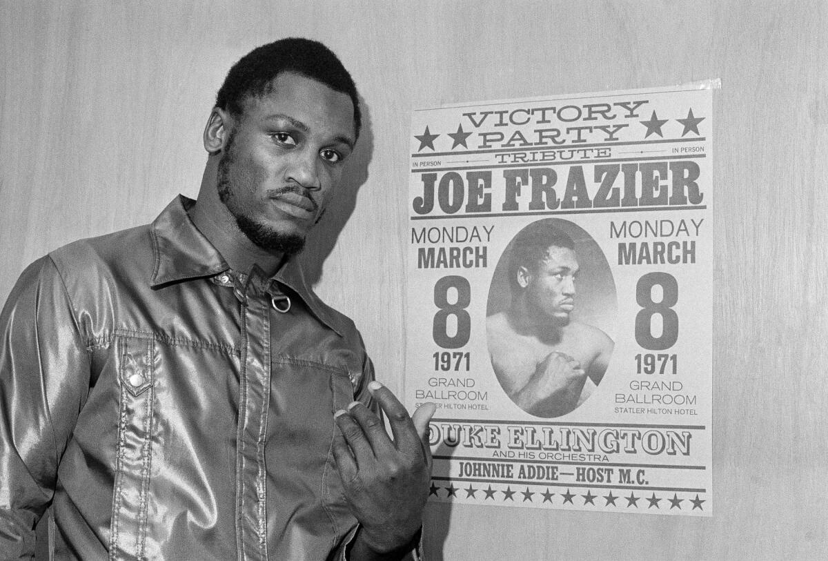 Joe Frazier poses by a poster advertising his "victory party" as he leaves his dressing room after a final public workout.