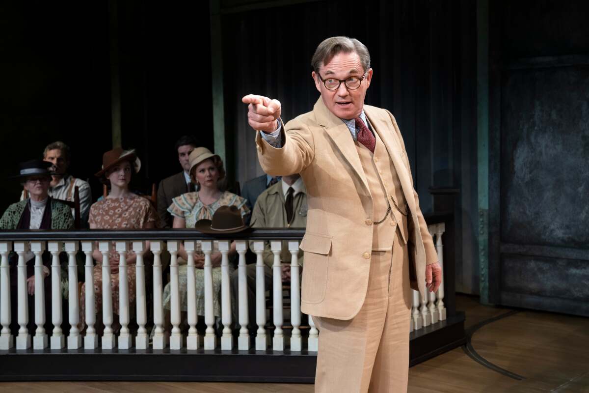 A lawyer in an old-fashioned beige suit and black-rimmed glasses points across the room in "To Kill a Mockingbird."