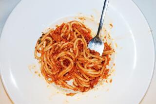 An overhead of a fork in a partially eaten white bowl of spaghetti in tomato sauce on a white tablecloth at Osteria Mamma.