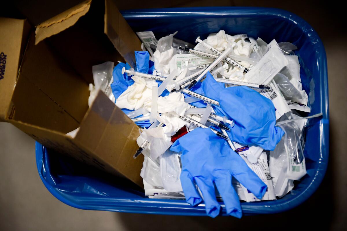 A trash bin filled with discarded gloves, syringes and other items