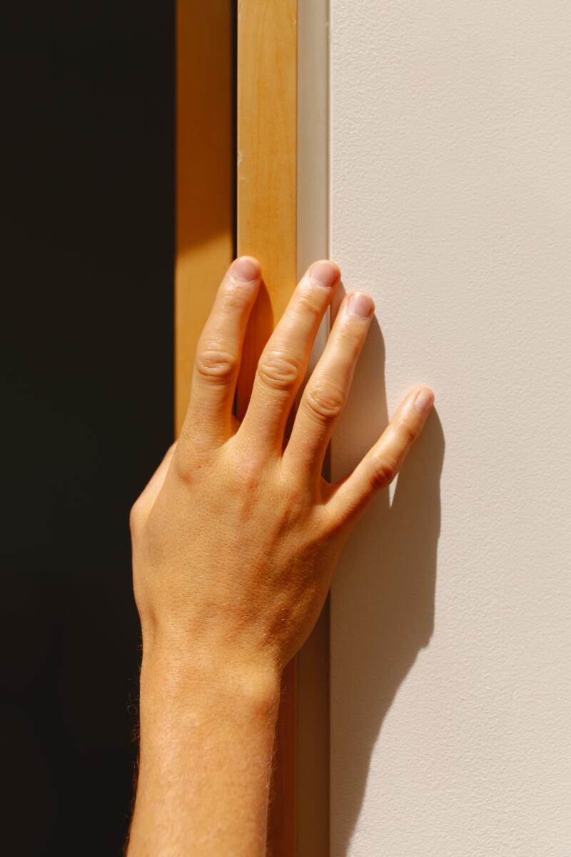 A hand rests on a door frame.