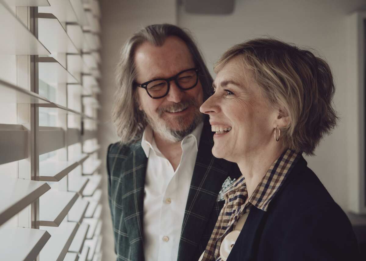 Gary Oldman and Saskia Reeves have a laugh looking out a window for a portrait.