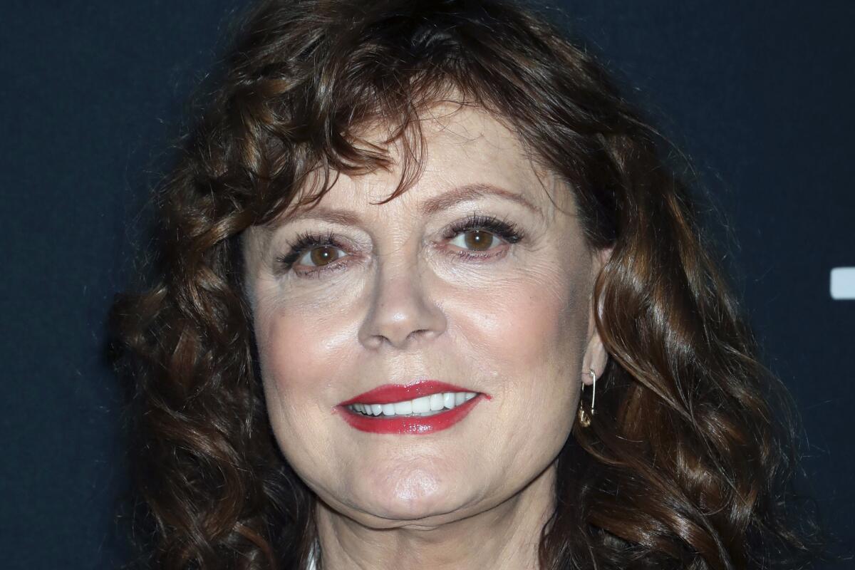 A closeup headshot of a smiling woman wearing red lipstick.