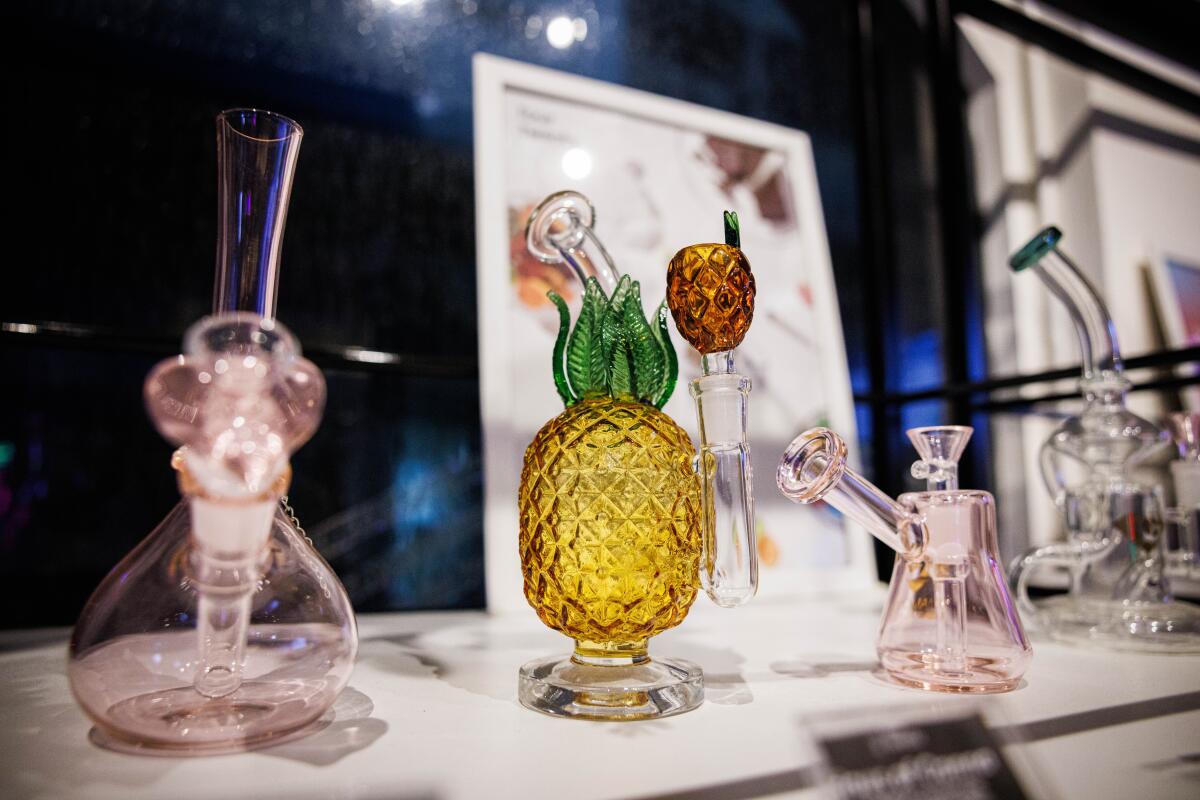 Bongs in clear pink and one shaped like a pineapple sit on a counter 