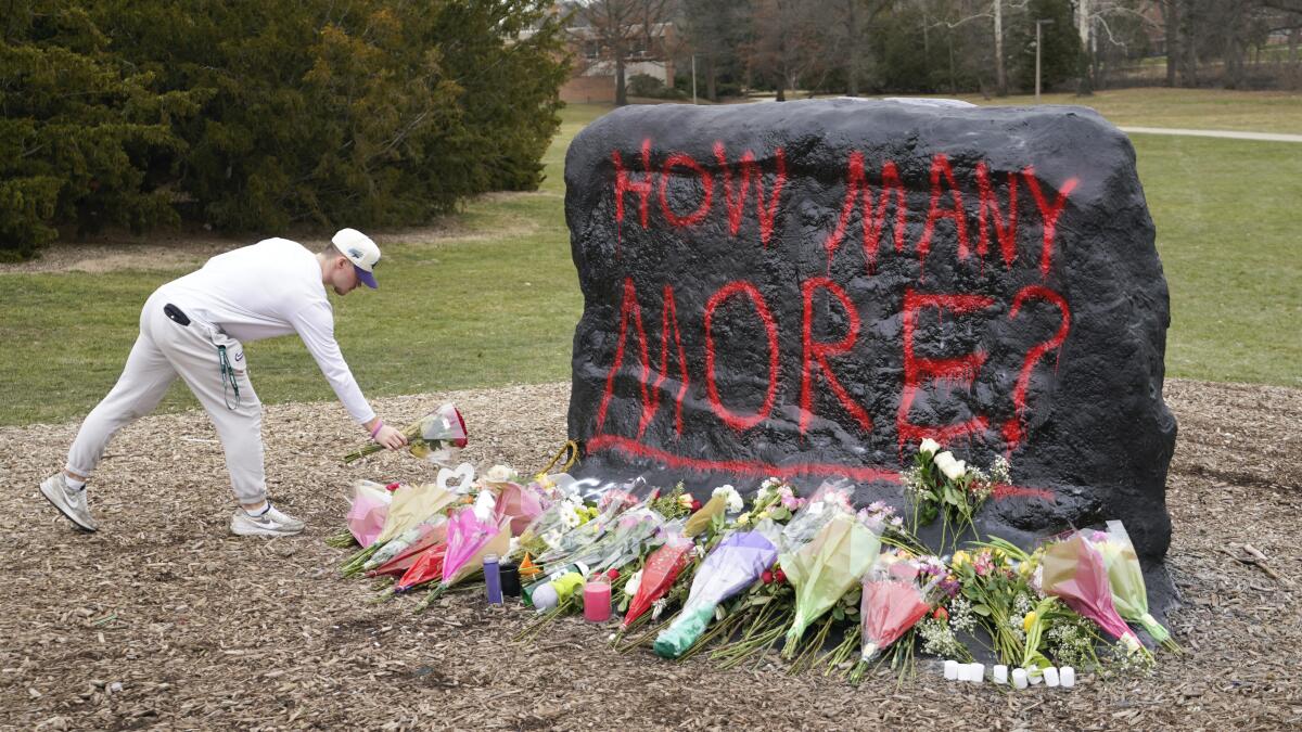 A student leaves flowers at a large rock painted with the words "How many more?"