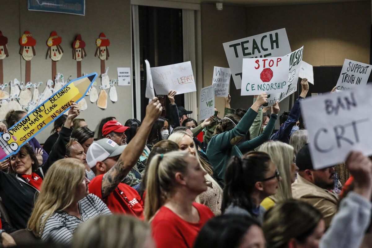 A mix of people hold up signs at a public school board meeting.