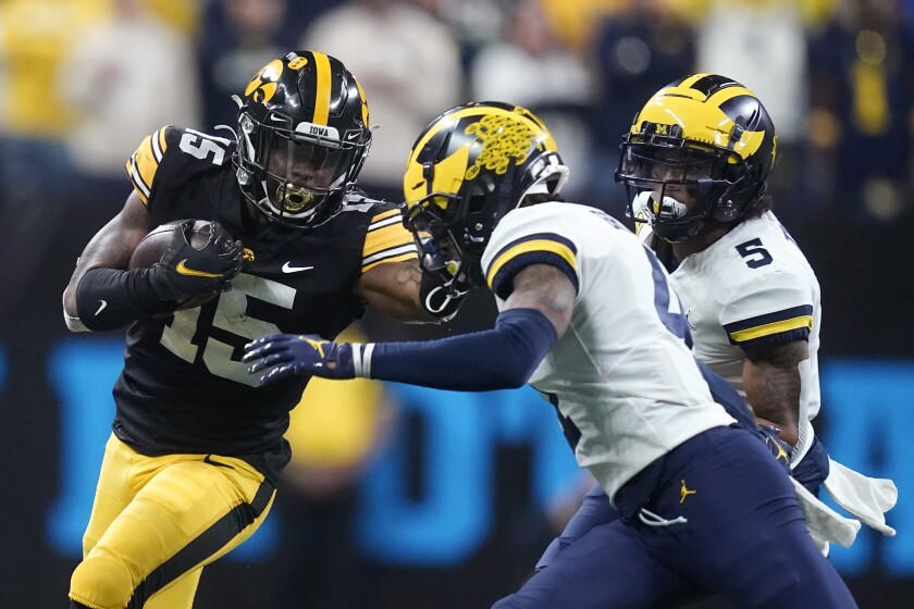 Iowa running back Tyler Goodson (15) runs from Michigan defensive back Vincent Gray, center, and defensive back DJ Turner (5) during the second half of the Big Ten championship NCAA college football game, Saturday, Dec. 4, 2021, in Indianapolis. (AP Photo/Darron Cummings)